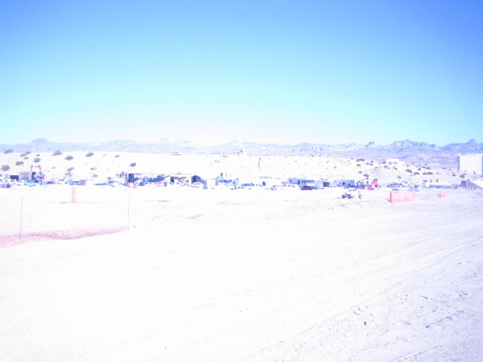 Distant desert race pit camps below mountains across a wide dirt course