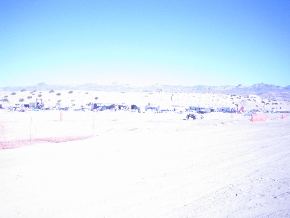 Desert race pit area with camps and orange fencing below a mountain range
