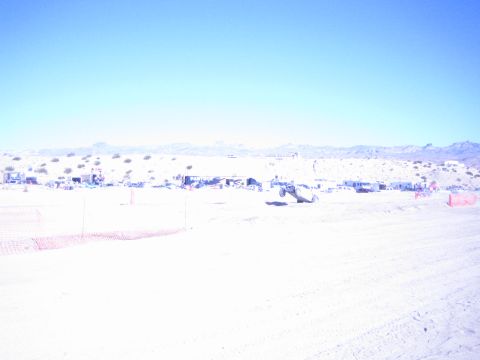 1990 Ford Bronco - offroad buggy crosses a sun-bleached desert race course past a long line of distant pit camps and vehicles.