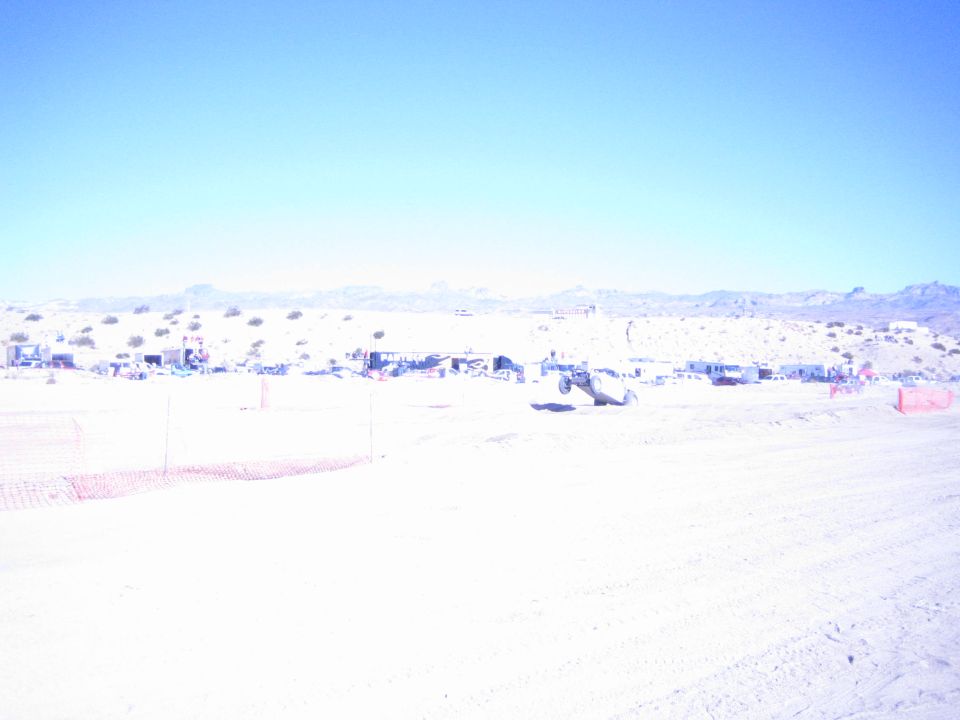 Offroad buggy crossing a bright desert course past distant pit camps