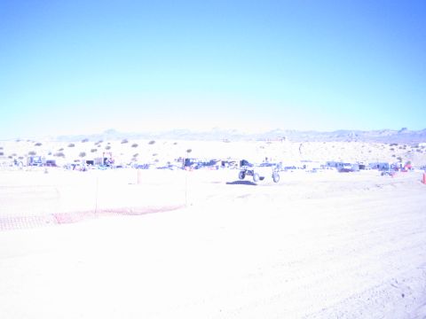 1990 Ford Bronco - offroad buggy runs along a washed-out desert course as pit camps and orange fencing line the background.