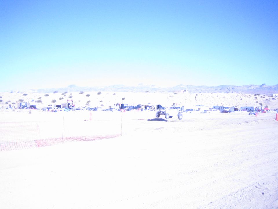Offroad buggy on a bright desert race course with pit camps behind fencing