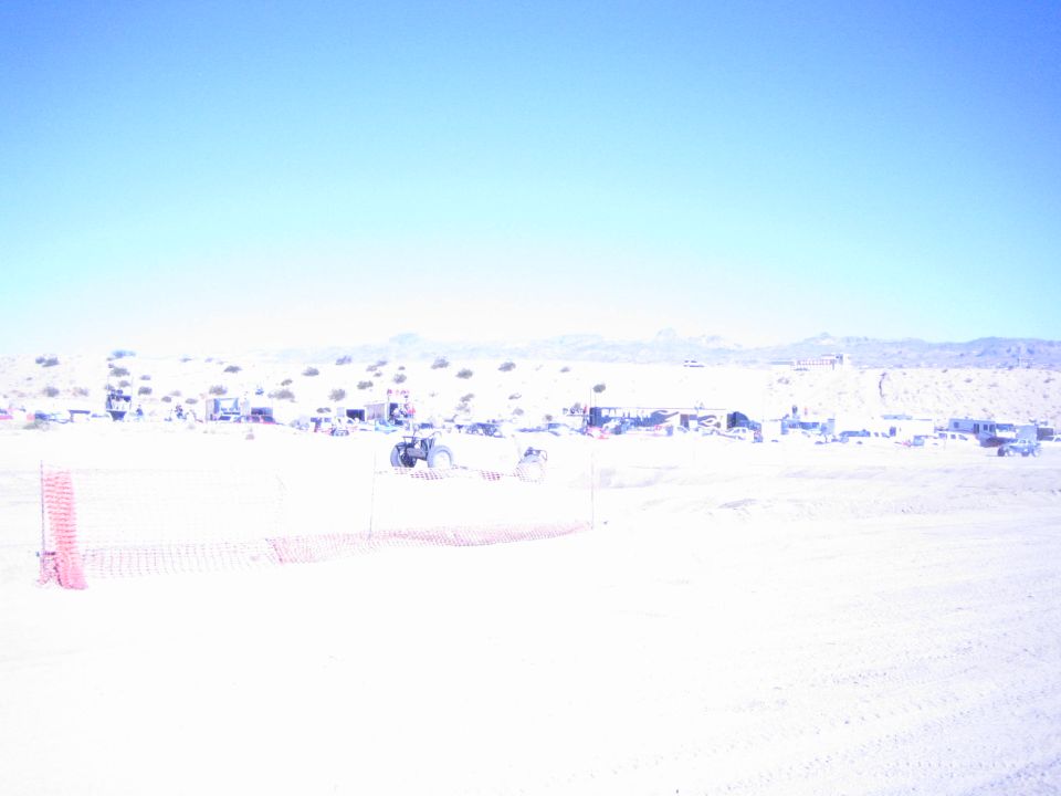 Offroad vehicle behind orange fencing on a bright wide desert race course