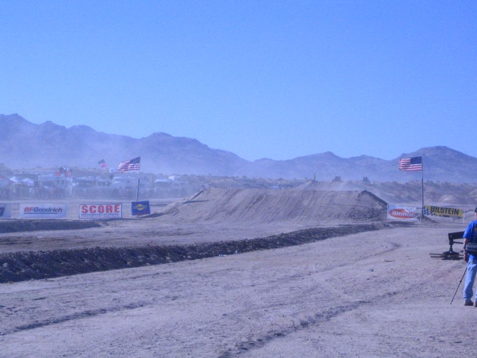 Desert race course with dirt berm, sponsor banners and a man watching