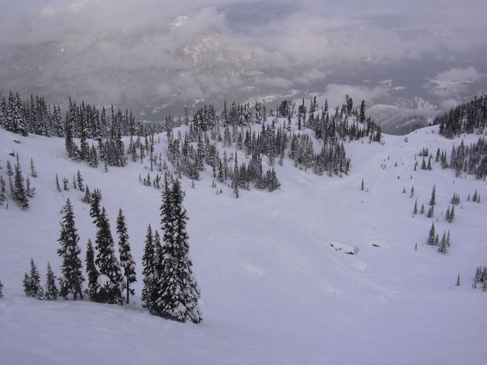 Snowy mountain landscape with pine trees and clouds in the distance. Supermotors.net logo in the corner