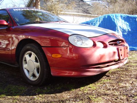 1997 Ford Taurus - The front end of a red sedan is visible, a white hood and a blue tarp behind it.