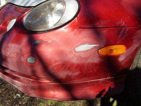 1997 Ford Taurus - Close-up of a red car's front bumper and headlight, showing areas prepared for repair.