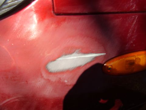 1997 Ford Taurus - Close-up of a red car fender showing a section of primer and an orange turn signal light.