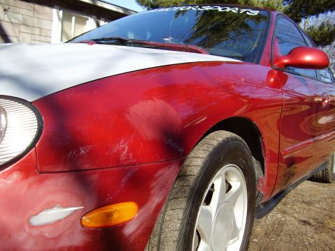 1997 Ford Taurus - Front quarter view of a red 1997 Ford Taurus with a primer-painted hood.
