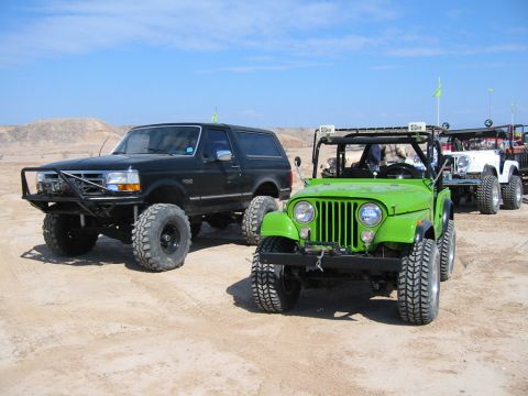 1992 Ford Bronco - Several off-road vehicles are lined up on a sandy terrain under a clear blue sky.