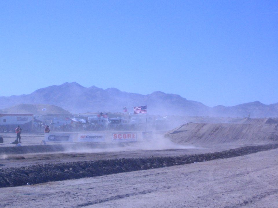Dusty desert race course with SCORE and BFGoodrich banners and US flags below mountains