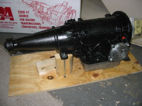 1985 Ford Crown Victoria LTD - A black transmission is displayed on a wooden platform, with a box showing a transmission diagram in the background.