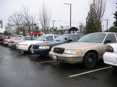 1999 Ford Crown Victoria - Multiple police sedans, including a tan Ford Crown Victoria, are parked in a lot on a cloudy day.