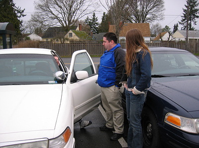 1999 Ford Crown Victoria - Two Ford Crown Victorias, a white one and a dark blue one, are parked next to each other with people standing between them.