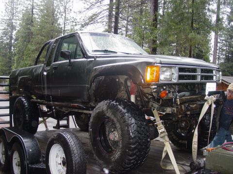 1986 Ford Bronco - A heavily modified pickup truck with large off-road tires is loaded onto a trailer.