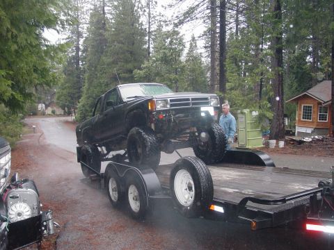 1986 Ford Bronco - A heavily modified black pickup truck is loaded onto a trailer, ready for transport.