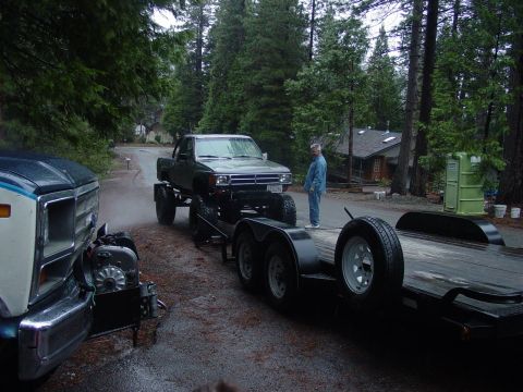1986 Ford Bronco - A lifted pickup truck is being towed on a trailer, with another truck visible in the foreground.