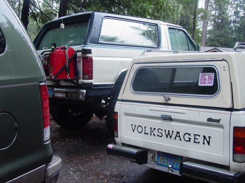 1986 Ford Bronco - A white Ford Bronco with a blue stripe and a red gas can is parked next to a Volkswagen pickup truck.