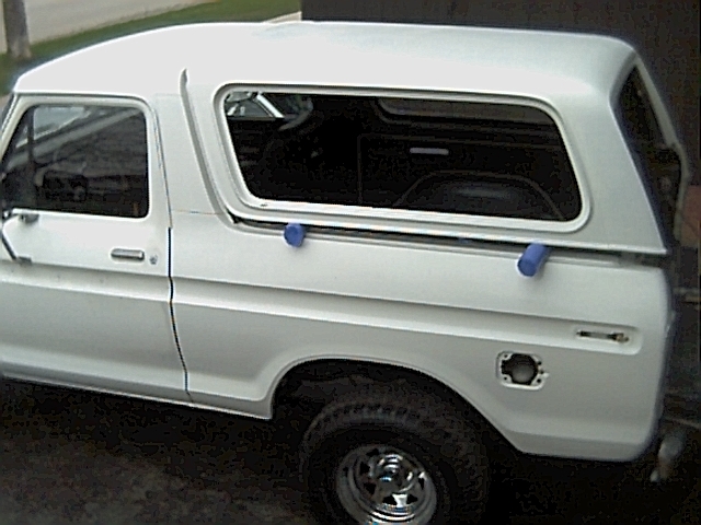 White 1978 Ford Bronco with camper shell, side view, showing dented fuel door area