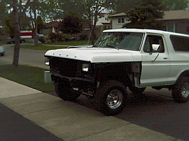 White 1978 Ford Bronco with black grille and missing fender, parked on a suburban street