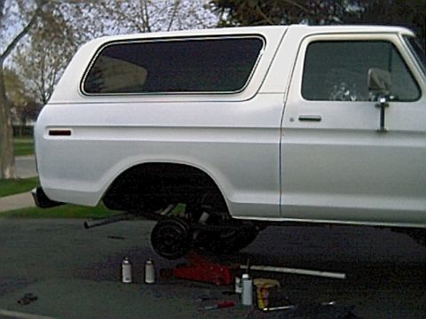 1978 Ford Bronco - A white 1978 Ford Bronco is shown with its rear wheel removed, indicating maintenance or repair work.