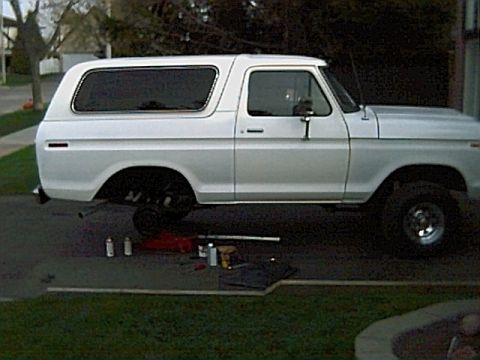 1978 Ford Bronco - A white 1978 Ford Bronco is shown from the side, with its rear wheel off and tools laid out nearby.