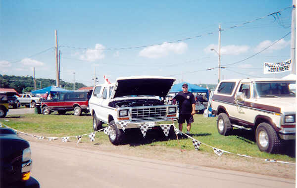 White 1978 Ford Bronco with hood open, man standing next to it. Another Bronco is parked to the right