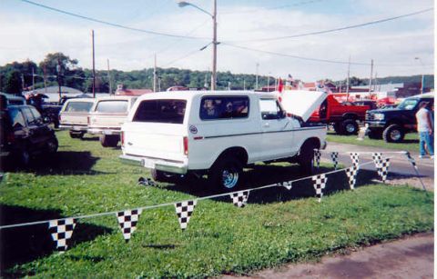 1978 Ford Bronco - A white 1978 Ford Bronco is displayed outdoors with other vehicles and checkered flags.
