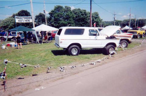 1978 Ford Bronco - A white 1978 Ford Bronco is parked at an outdoor event, with a banner overhead reading "Project Bronco Meets Here!".