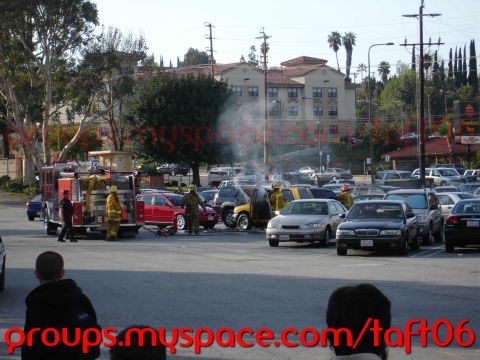 1993 Ford Taurus - Emergency responders work to extinguish a vehicle fire in a crowded parking lot.