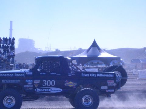 1990 Ford Bronco - Side view of blue off-road race truck number 300 lettered Cinnamon Ranch and River City Differential on a desert course.