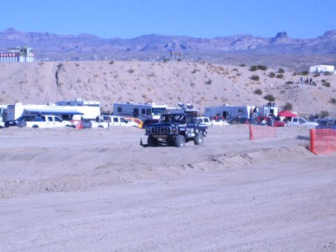 1990 Ford Bronco - dark off-road truck on a desert dirt course, with a hilltop casino building and rocky mountains in the background.