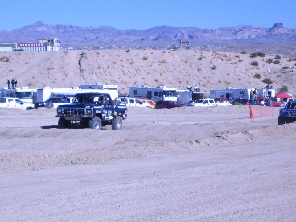 Dark off-road race truck on a desert dirt course with RVs and casino behind