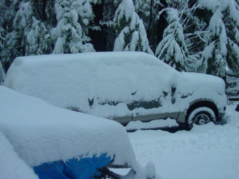 1986 Ford Bronco - A snow-covered SUV sits parked outdoors amidst a winter scene with snow-laden trees in the background.