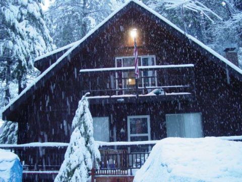 1986 Ford Bronco - A dark wooden cabin is covered in snow during a winter storm, with snow falling heavily.
