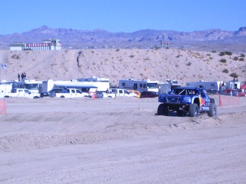 1990 Ford Bronco - blue Red Bull-liveried off-road truck on oversized tires runs a desert dirt course past parked RVs.