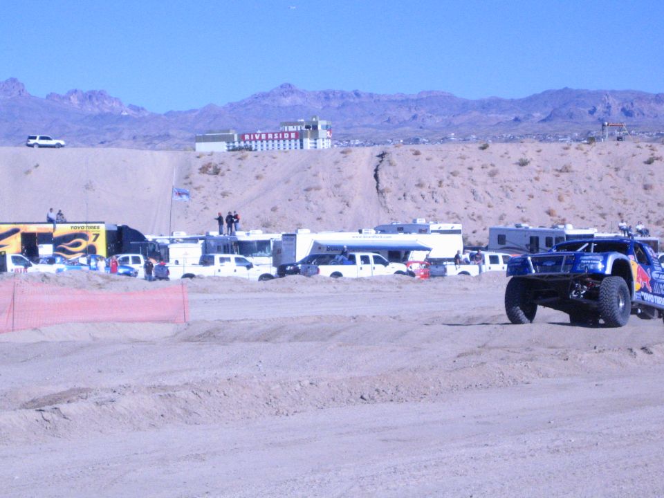Blue off-road truck at right on a desert course near a yellow Fabtech banner