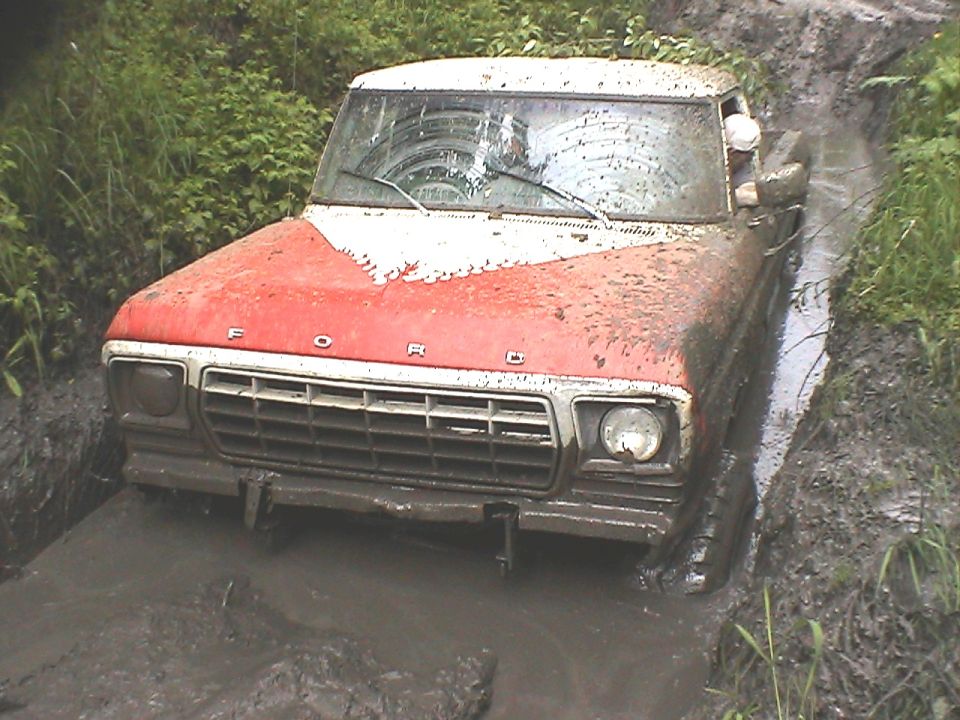 1979 Ford F-150 stuck in a muddy rut, front view. Red and white paint is covered in mud