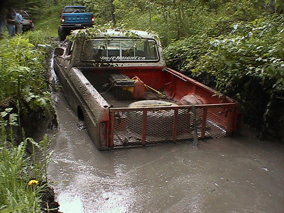 Muddy pickup truck stuck in a ditch with a blue Dodge truck behind it