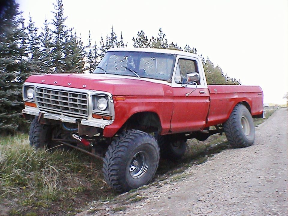 Red and white 1979 Ford F-150 pickup truck with large tires, parked on a dirt road