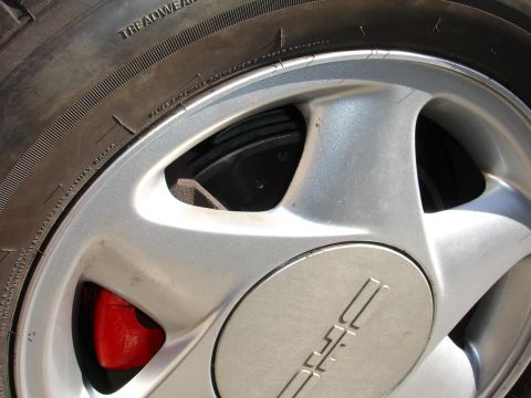 1993 Ford Taurus - Close-up of a red brake caliper peeking through a silver alloy wheel, showing part of the tire tread.