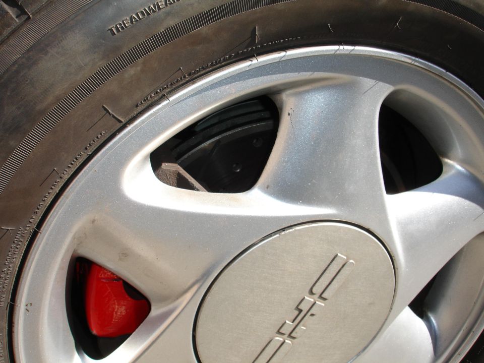 Red brake caliper visible through silver alloy wheel with a stylized logo