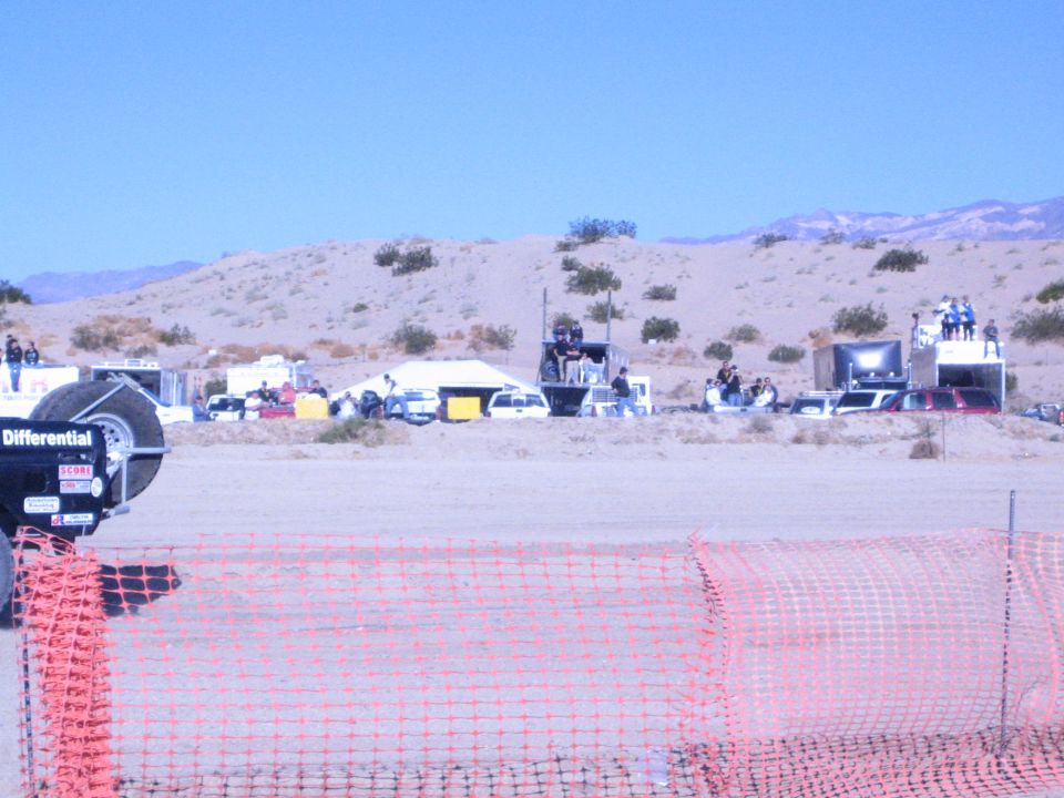 Desert race pit area with trailers and a black tire-cover reading Differential behind orange fence