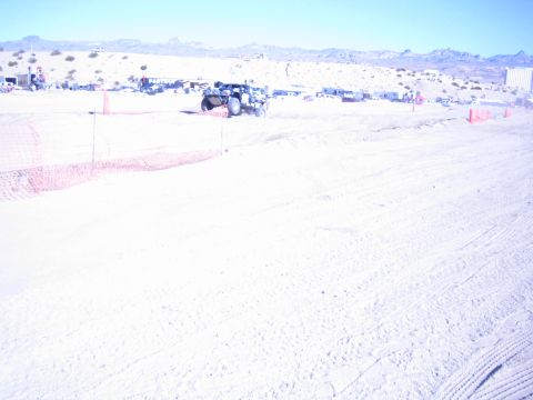 1990 Ford Bronco - lone off-road vehicle kicks up dust on a wide, sun-bleached desert race course lined with orange fencing.
