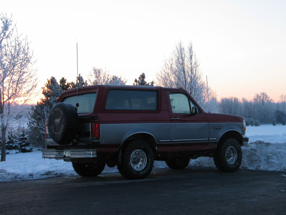 Red and silver 1995 Ford Bronco with spare tire on rear, parked in snow