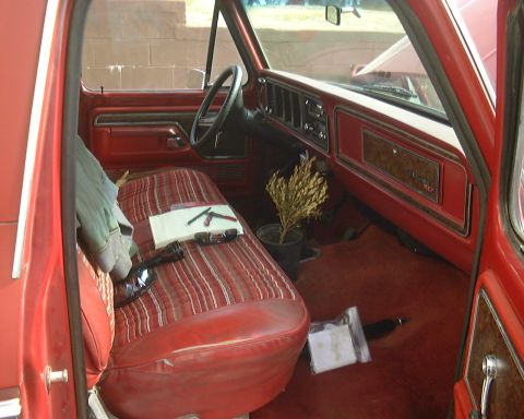 1978 Ford Bronco - The interior of a 1978 Ford Bronco shows red striped seats, wood grain dashboard accents, and a small potted plant.