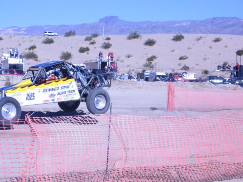 1990 Ford Bronco - yellow off-road buggy numbered 1625 with Dennco Trim and Euro Tech livery races a desert course past orange fencing.