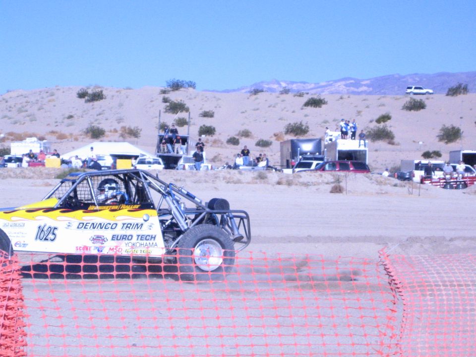Yellow off-road buggy number 1625 on a desert course with spectators on platforms