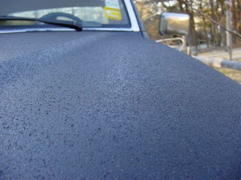 1989 Ford Bronco - A close-up view of a dark blue textured hood, with a chrome side mirror in the background.