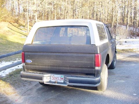 1989 Ford Bronco - Rear view of a dark blue and white Ford Bronco parked outdoors with trees in the background.